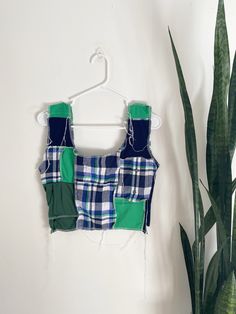 a green and blue patchwork top hanging on a wall next to a potted plant