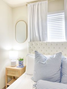 a bed with blue and white pillows in a bedroom next to a mirror on the wall