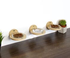 three wooden bowls with food in them on a shelf next to a potted plant