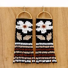 two wooden hoop earrings with white and brown beads on them hanging from a wood wall