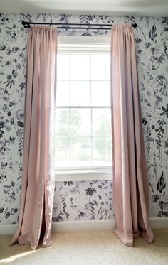 a pink curtain hanging in front of a window with floral wallpaper on the walls