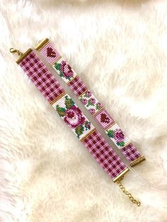 a pink and white bracelet with roses on it sitting on top of a furry surface