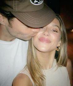 a man kissing a woman's face while wearing a baseball cap and white tank top