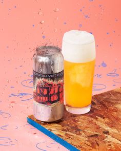 a glass of beer sitting on top of a wooden table next to a metal can