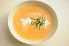 a bowl of soup with sour cream and chives in it on a white table