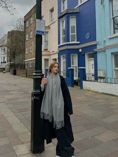 a woman standing next to a pole on the side of a street with buildings in the background