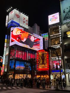 people are standing in the middle of a busy city street at night with brightly lit buildings and billboards