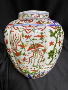 a white vase with red and green designs on it's sides sitting on a black background