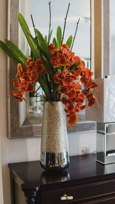 a vase filled with orange flowers sitting on top of a table next to a mirror