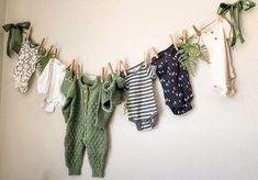 baby clothes hanging on a clothes line with green leaves and plants in them, against a white wall