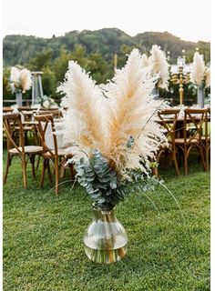 a vase filled with flowers sitting on top of a lush green field next to wooden chairs