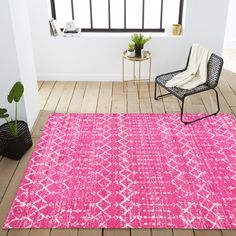 a bright pink area rug with white and black designs on the floor next to a chair