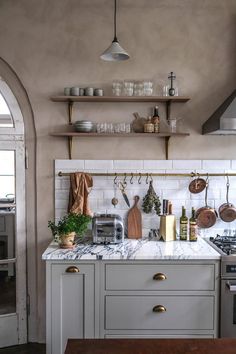 a kitchen with marble counter tops and wooden shelves above the stove top is filled with cooking utensils