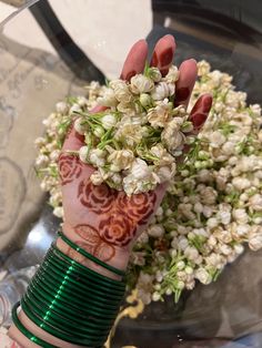 a woman's hand with henna and bracelets on her wrist holding flowers