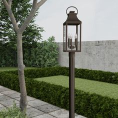 a lamp post with two lit candles on it in the middle of a garden area