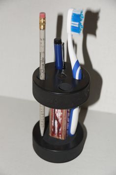 two toothbrushes are sitting in a holder with pencils and markers on it