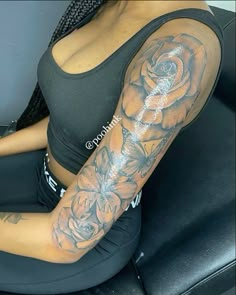 a woman is sitting in a chair with tattoos on her arm and shoulder, she has a rose tattoo on her arm