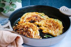 an iron skillet filled with cabbage covered in seasoning next to a potted plant