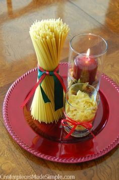 a red plate topped with two vases filled with yellow spaghetti and one lit candle