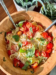 a wooden bowl filled with pasta, tomatoes and basil garnished with parmesan cheese