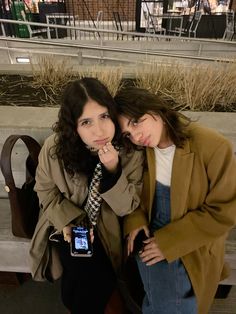 two women are sitting on a bench and posing for the camera