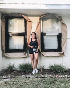 a woman standing in front of a house with her hands on the window sill