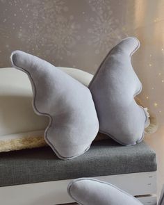 two pillows sitting on top of a white bed next to a pillow with the shape of an angel's wings