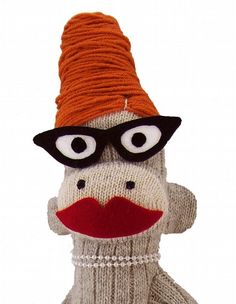 a sock monkey wearing glasses and a knitted hat is posed in front of a green background