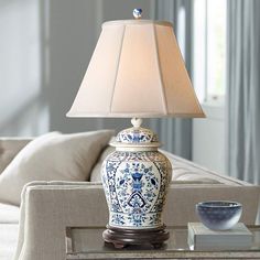 a blue and white lamp sitting on top of a glass table next to a couch