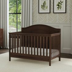 a baby crib in a room with two pictures on the wall and curtains behind it