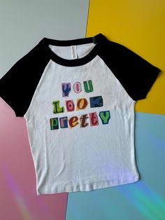 This is a SUPER CUTE and trendy cropped baby tee with black sleeves and a quote saying "you look pretty" in magazine cut out style.  Designs  are sublimated on a soft bella canvas shirt making it super high quality and comfy.  Washing: Machine was cold inside out to prevent fading!  *this is a one of one item only one is available currently in a size extra small. all items are handmade!  *if you are looking for a different size or color please feel free to reach out for custom orders (subject to an additional charge)*  *if you have any comments, suggestions, or concerns please do not hesitate to reach out 90s Inspired Text Print T-shirt For Spring, Fun Pink Top With Graphic Design, Playful Graphic Tops For Streetwear, Cute Graphic Design Tops For Summer, Cute Graphic Design Tops For Spring, Fun Graphic Design Tops For Spring, Fun Spring Graphic Design Tops, 90s Inspired Letter Print T-shirt For Spring, 90s Inspired Funny Print T-shirt For Spring