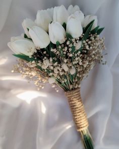 a bouquet of white tulips and baby's breath on a white sheet