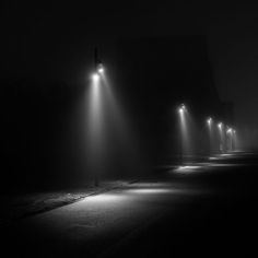 several street lights in the dark on a foggy night with no one around them