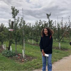 two women standing in an apple orchard with trees and signs on the side of the road