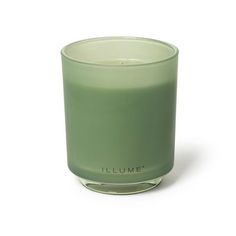 a green candle is sitting on a white surface with the words illume written in black