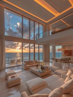 a living room filled with lots of white furniture and large windows overlooking the ocean at sunset