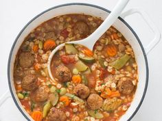 a pot filled with meatballs and vegetables on top of a white countertop next to a wooden spoon