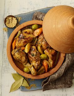 a bowl filled with meat and vegetables next to a wooden spoon on top of a table