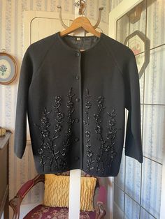 This beautiful sweater is made from a medium weight wool blend in pure black, with gorgeous floral beading in black and amber on the front. It has the original covered buttons and is fully lined. Marked size 44. The measurements, taken with the sweater lying flat, are: shoulder to shoulder, 18 inches; armpit to armpit, 22 inches; sleeves, 20 inches; length, 24 1/2 inches; bottom edge, 24 inches. In very good condition. Elegant Black Wool Cardigan, Vintage Black Fitted Sweater, Elegant Black Crew Neck Outerwear, Vintage Black Sweater For Spring, Fitted Embroidered Sweater For Fall, Black Vintage Sweater For Spring, Elegant Embellished Sweater For Fall, Black Crew Neck Sweater For Evening, Elegant Embroidered Winter Cardigan