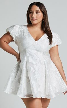 a woman wearing a white dress with ruffled sleeves and short legs, posing for the camera