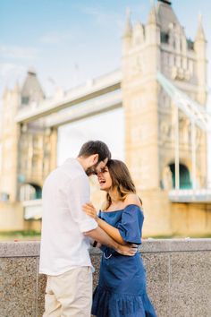 an engaged couple standing in front of the tower bridge