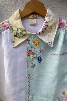 a white shirt with colorful flowers on it and a wooden hanger hanging from the wall