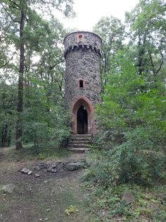 an old stone tower in the woods with stairs leading up to it's entrance