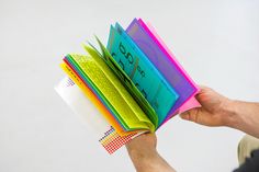 a person holding an open book with colorful papers on top of it and the pages folded in different colors