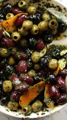 olives and peppers in a white bowl on a marble counter top with herbs sprinkled over them