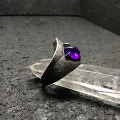 I set out to create a series of rings that looked as if they were roughed out of stone, fit for royalty in an early age of mankind. Set with a 10x8mm deep purple colored amethyst. The sterling silver band is hand carved and textured with a primitive and raw multidirectional pattern, each mark was imbued with intent and energy for protection of its wearer. I then oxidized and hand sanded to 400 grit to show the pattern and shine the metal. Brought back for a limited series run. Modern Purple Metal Jewelry, Gothic Hand Cast Ring Jewelry, Fantasy Style Amethyst Purple Jewelry, Fantasy Style Purple Amethyst Jewelry, Purple Amethyst Fantasy Jewelry, Hand Forged Round Amethyst Jewelry, Hand Forged Adjustable Purple Jewelry, Hand Forged Amethyst Ring As Gift, Purple Amethyst Hand Forged Jewelry