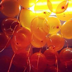 many balloons are floating in the air with string attached to them and some oranges hanging from the ceiling