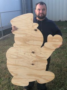 a man standing in front of a wooden snowman cutout on the grass holding it up