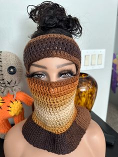 a mannequin wearing a knitted mask with hair in the top knot and two stuffed animals behind it