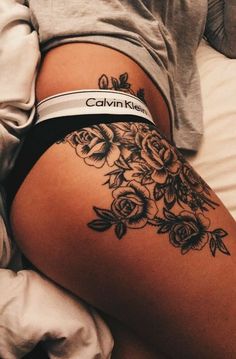 a woman laying in bed with flowers on her thigh and tattoos on her butts